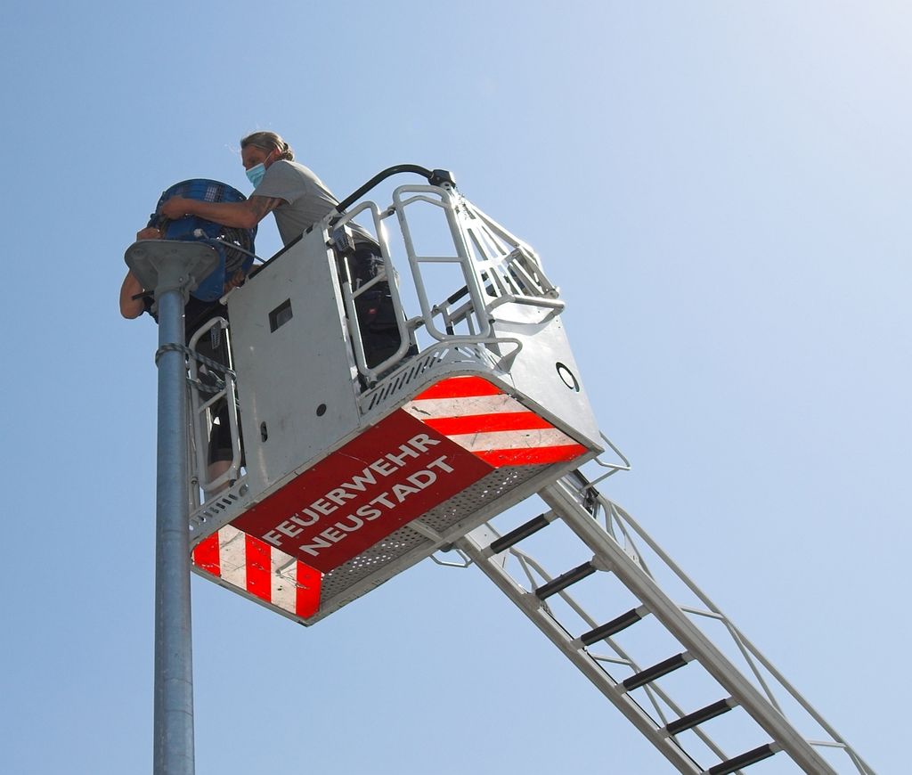 Das Foto zeigt, wie mit vereinten Kräften die Sirene auf die Montageplatte gehoben und ausgerichtet wird.